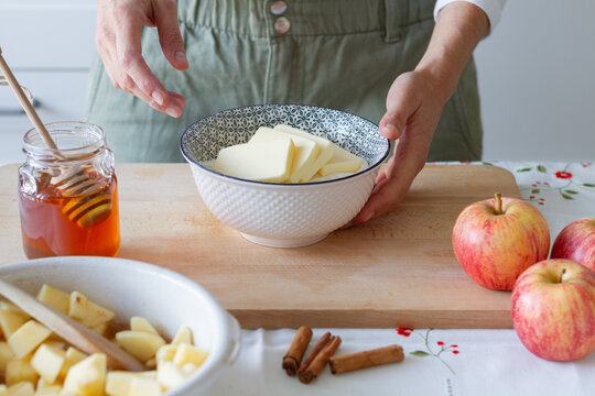 Unrecognizable person mixing butter with flour in bowl while preparing dough for crumble near butter and apples with cinnamon on table at home