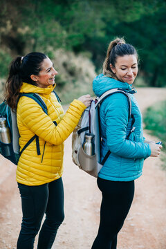 Side view of positive hiker fastening backpack of female friend while standing on sandy road in nature during trekking