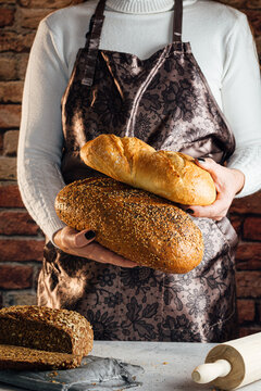 Faceless female artisan in apron with different types of bread with golden crust and sunflower seeds