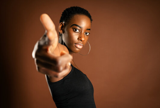 African American female with trendy earrings pointing at looking at camera against brown background