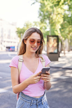 Young woman walking on pedestrian crossing and checking route on mobile phone in Madrid