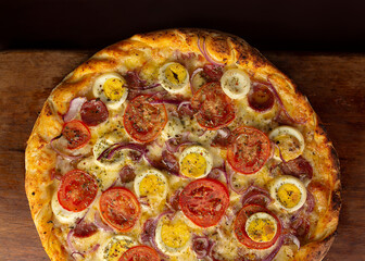 Top view of isolated pizza with cheese, pepperoni, eggs, tomato, onion and bacon or baiana, on wooden board 