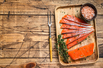 Salted salmon fillet slices in a wooden tray with thyme. wooden background. Top view. Copy space