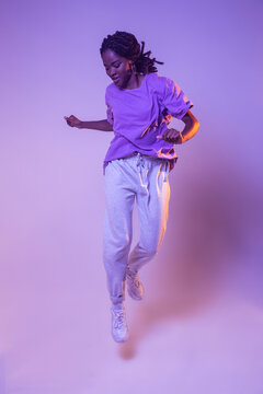 Full body of dynamic African American teen dancer leaping up while performing dance movement in bright studio