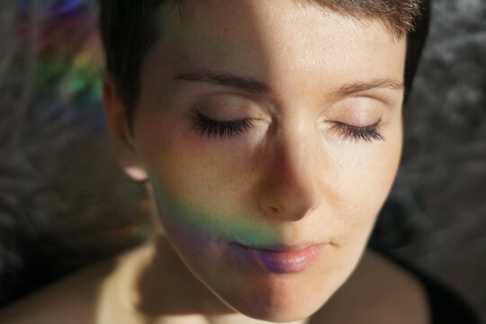 Crop feminine thoughtful adult lady with natural makeup and short hair smiling with eyes closed dreamily in sunlight