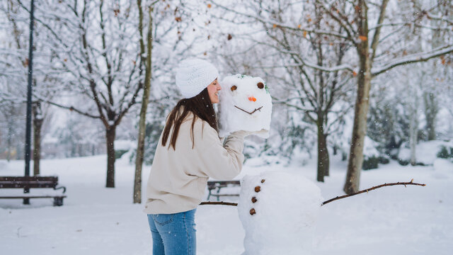 Side view of young cheerful female with snowman head in park with leafless trees in wintertime