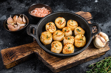 Fried scallops with butter sauce in a pan. Black background. Top view