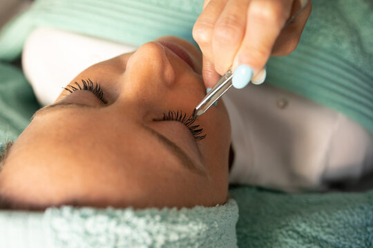 High angle of crop unrecognizable cosmetician using tweezers while preparing eyelashes of female client for lamination