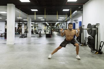 Full body of strong young muscular male athlete in activewear lifting barbells during intense workout in modern gym