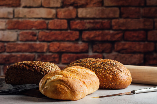 White and rye bread with cereals and appetizing crust on cutting board against brick wall in bakehouse