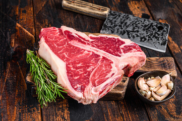 Raw T-bone beef meat Steak with herbs on a wooden cutting board. Dark wooden background. Top view
