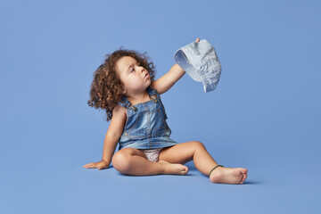 Adorable upset little kid with brown eyes wearing casual clothes and hat against blue background looking away
