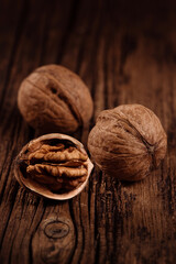 Three ripe walnuts on textured wood brown background. Closeup. Selective focus.