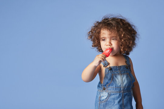 Unemotional thoughtful little girl standing with melting popsicle against blue background