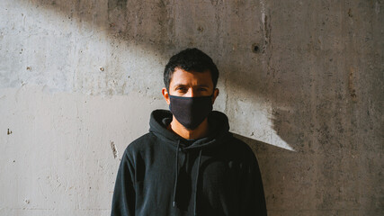 trendy guy in face mask looking at camera while standing on street near shabby wall on sunny day