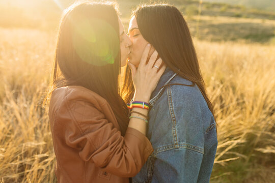 Side view of young lesbian couple standing in field and kissing tenderly with closed eyes