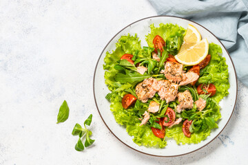 Salad with baked salmon fish. Green salad mix with tomatoes and salmon. Top view at white table.