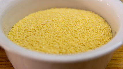 Close view of a bowl of raw couscous on top of a wooden table
