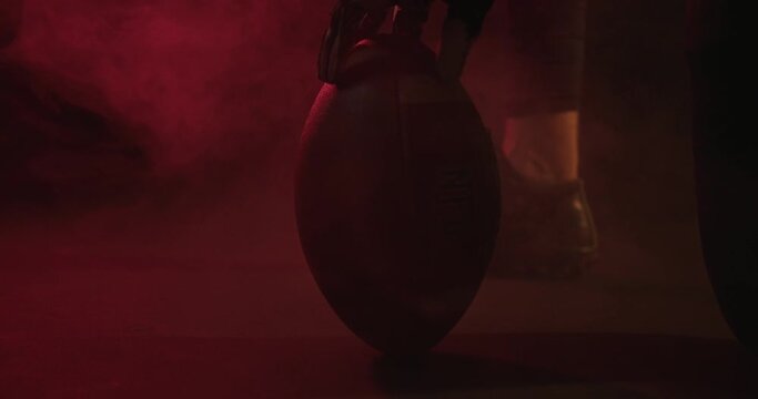 Crop rugby player with ball in dark studio. Unrecognizable male rugby player spinning ball in dark studio with red neon light and steam