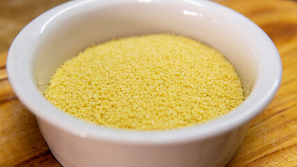 Close view of a bowl of raw couscous on top of a wooden table