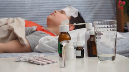 sick kid with runny nose and fever heat lying on couch at home, mom treats son, gives medicine, drinks pills, blows his nose.