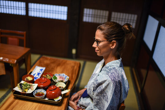 Young caucasian woman in a kimono sitting at the table in a traditional Japanese house