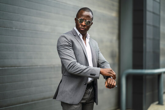 Masculine African American male executive in formal suit and sunglasses revising time on street