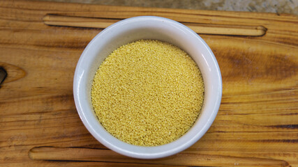 Close view of a bowl of raw couscous on top of a wooden table