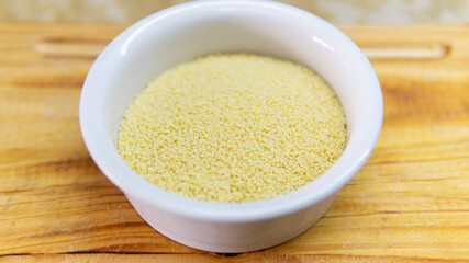 Close view of a bowl of raw couscous on top of a wooden table