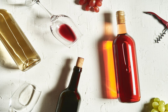 Top view arrangement of fine red and white wines lying on cracked surface amidst wineglasses and grapes