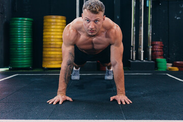 Focused male athlete with muscular naked torso doing push ups during functional workout and looking forward