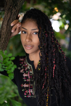 Portrait of attractive afro latina woman with dreadlocks standing by a tree