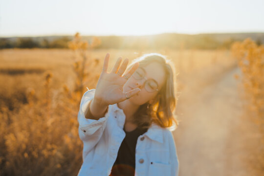 Front view of active young lady in trendy outfit showing hand in dry fiends against cloudless sky in countryside