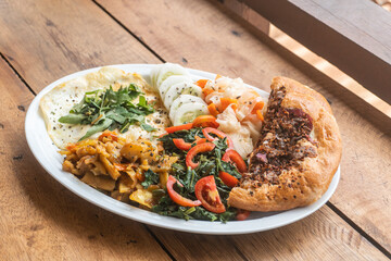 Jajka smażone z warzywami i pizzą, pyszne śniadanie na białym talerzu na drewnianym stole.