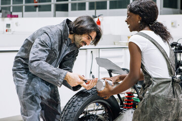 Delighted diverse technicians in workwear repairing muffler of custom motorbike while working together in bright workshop