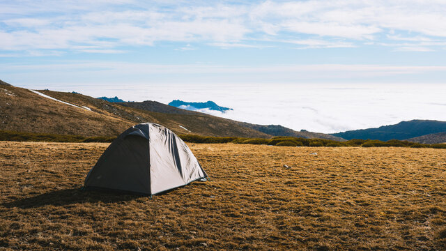 Picturesque scenery of camping tent placed on grassy hill slope in snowy mountainous valley against cloudy sky in sunlight