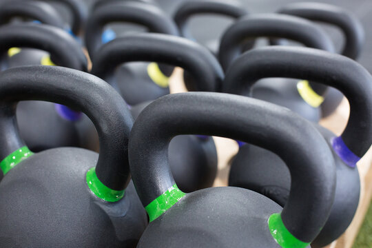 Full frame closeup of heavy black iron kettlebells with colorful weight labels arranged in rows in gym
