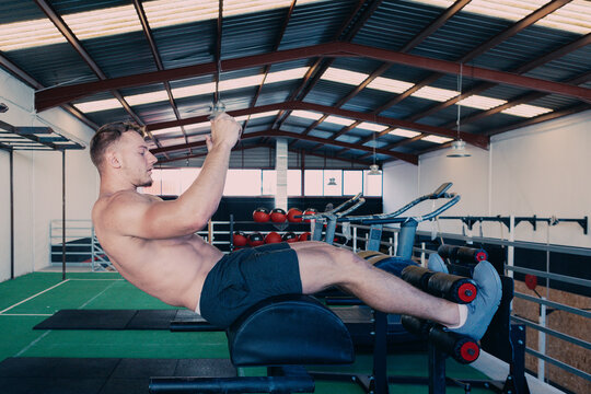 Side view of determined male athlete with naked torso doing abdominal crunches on bench during functional workout in gym