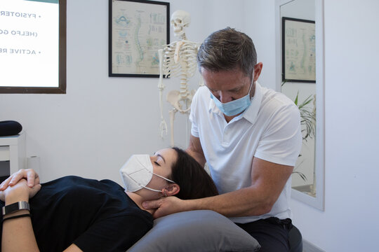 Unrecognizable male physiotherapist in face mask checking up neck of woman near human skeleton in medical center