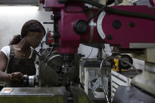 Side view of professional young African American female mechanic processing detail on lathe machine while working in repair workshop - Powered by Adobe