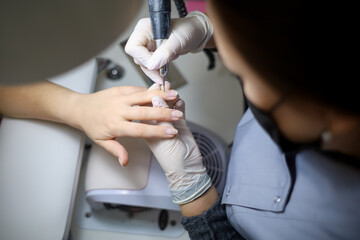 manicure master processes the client's nails with a nail grinding machine. A manicurist with a device in her hands grinds her nails making preparations for applying nail polish