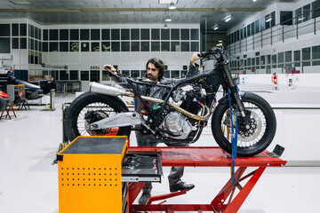 Professional male technician inspecting custom motorcycle while working in modern repair service workshop