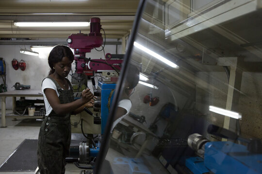 Side view of professional young African American female mechanic processing detail on lathe machine while working in repair workshop