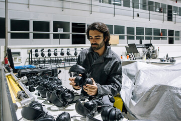 Professional male mechanic in workwear taking headset from shelf while preparing for repairing process in modern equipped workshop