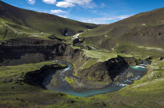 Amazing view of curvy blue river loop streaming on rough hilly terrain covered with lush abundant vegetation under majestic blue sky