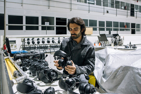 Professional male mechanic in workwear taking headset from shelf while preparing for repairing process in modern equipped workshop