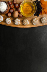 energy balls and ingredients for their preparation on a wooden board on a black slate background. nuts raisins coconut honey and dried apricots. recipe for a nutritious breakfast or snack