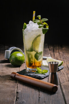 Glasses with cold alcohol Mojito cocktail with rum and fresh lime served with ice and mint leaves on wooden table with squeezer and jigger