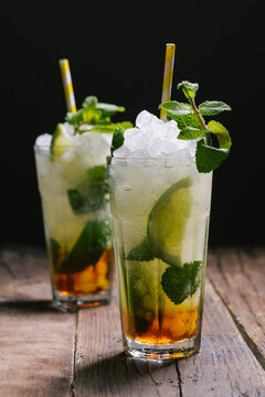 Glasses with cold alcohol Mojito cocktail with rum and fresh lime served with ice and mint leaves on wooden table