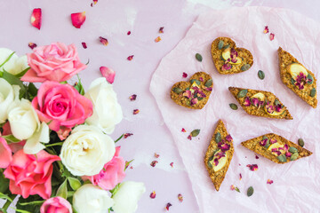 Homemade apple granola bars with dried apple and pumpkin seeds, lying on a pale pink background, decorated with a bouquet of pink and white roses, top view